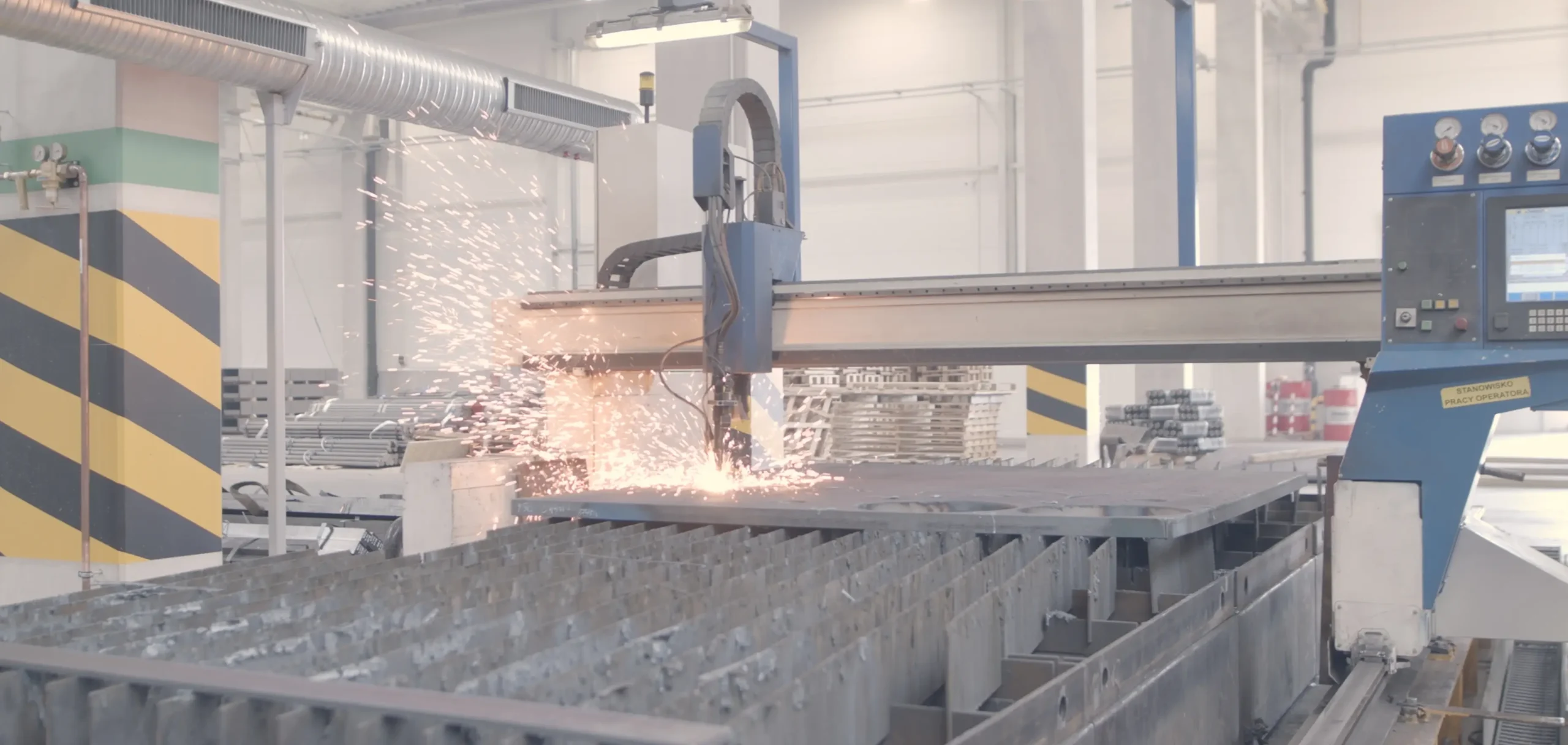 Maszyna CNC tnąca stalowe elementy w hali produkcyjnej, widoczne iskry podczas obróbki metalu.